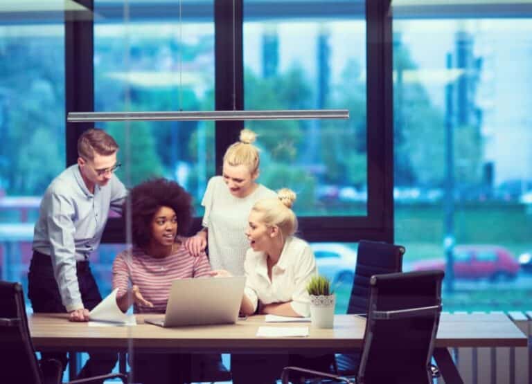 A group of young entrepreneurs sit at a desk and look at a laptop.