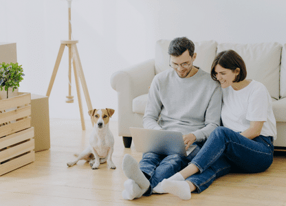 Ein junges Pärchen mit Hund sitzt am Computer.