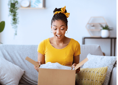 A woman sits on her couch and opens a package