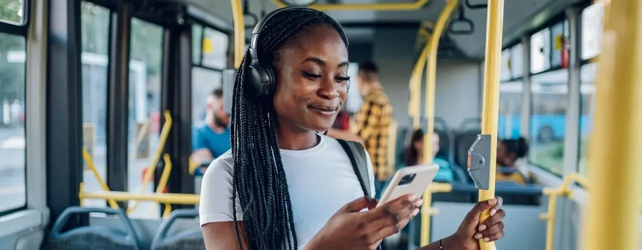 A woman inside a bus, listening to music and looking at her smarthpone. She's smiling.