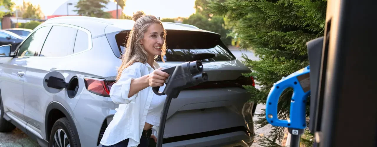 A woman plugs in an electric car plug into a charging station.