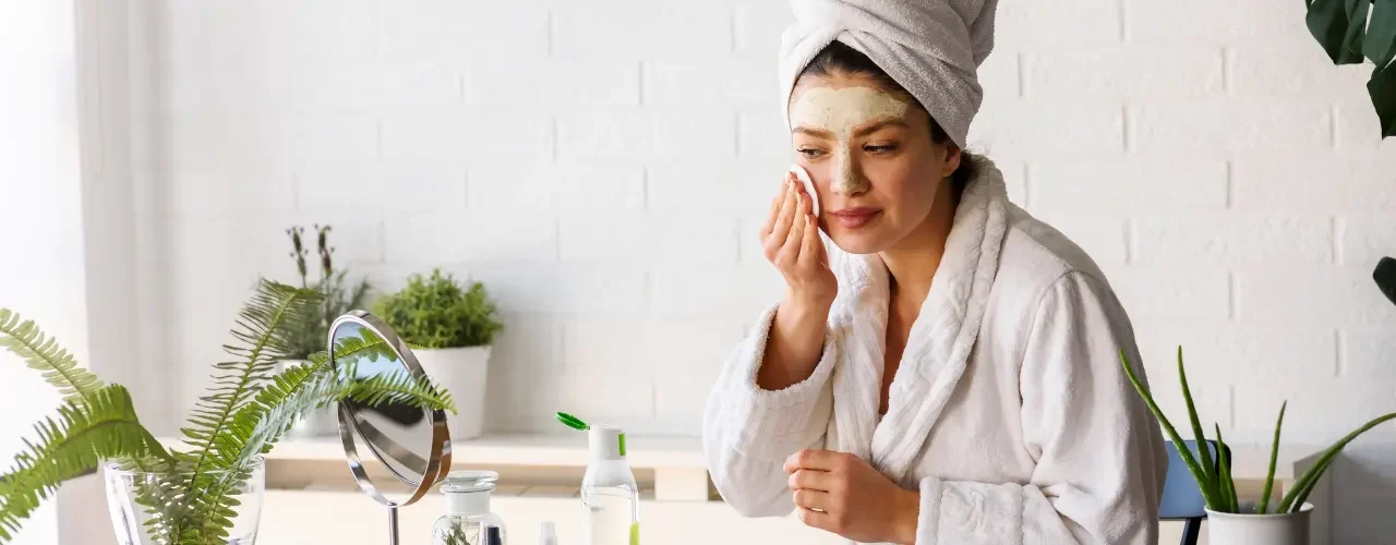 A women sits in front of a mirror and applies different beauty cremes to her face.