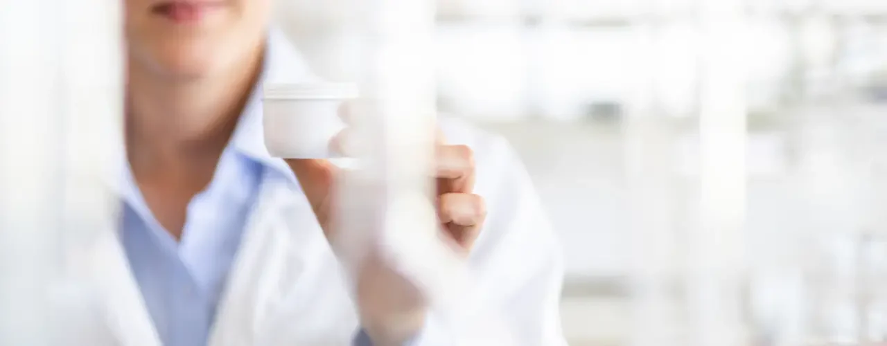 A scientist holding a pot of skin cream in a laboratory