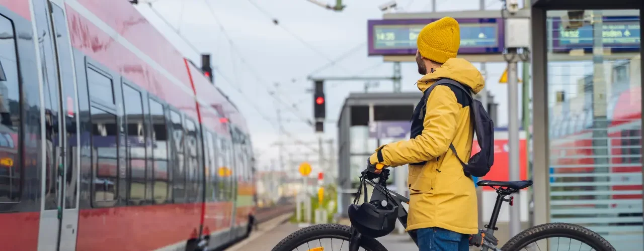A person in a yellow rain coat and a bike is waiting for a train.